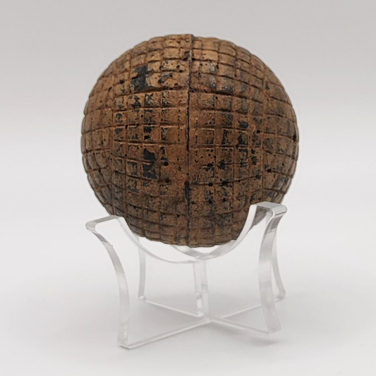 Antique gutta percha golf ball with grid pattern on a clear stand against a white background