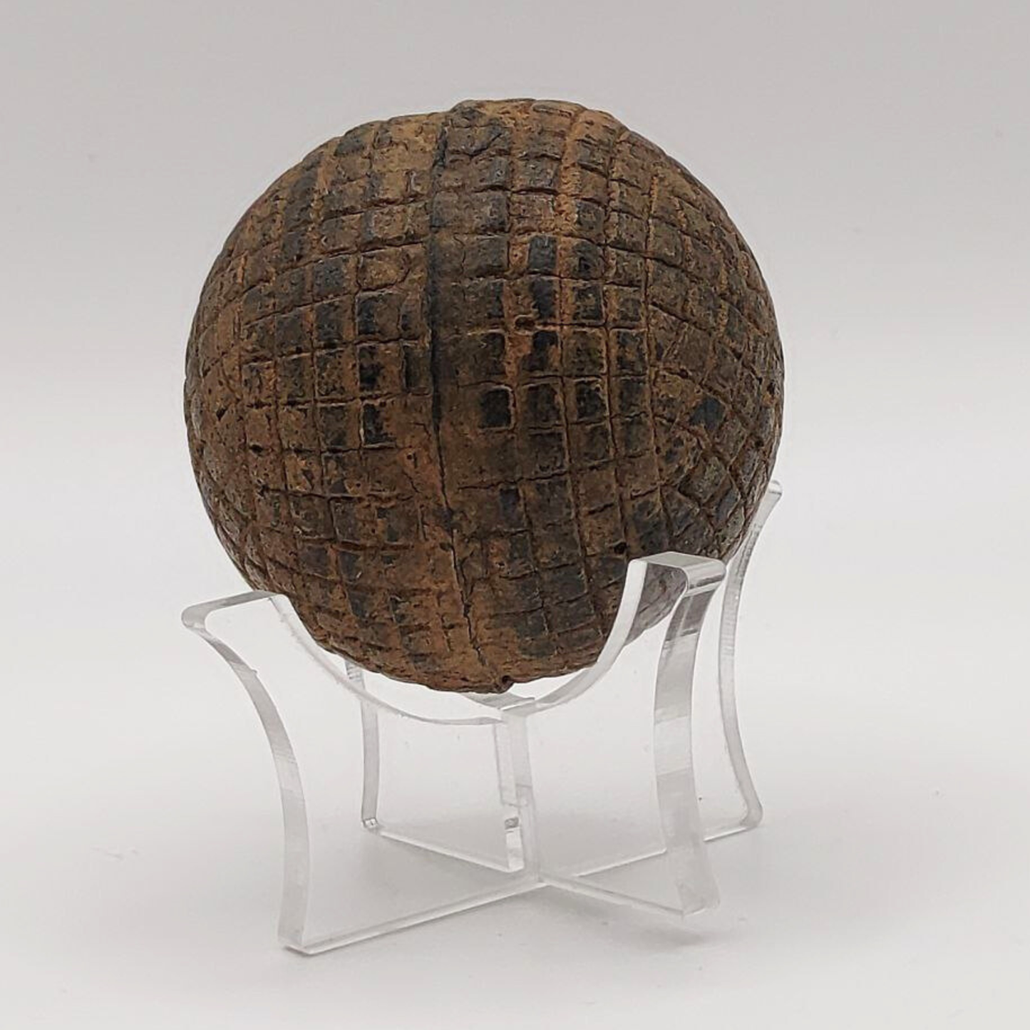Textured brown antique gutty golf ball on a clear stand against a white background