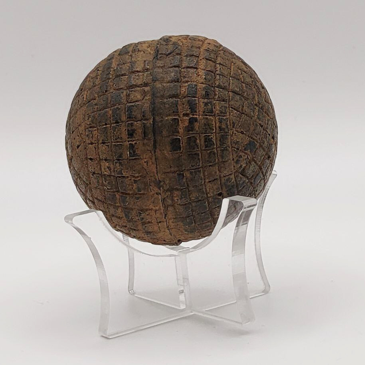Textured brown antique gutty golf ball on a clear stand against a white background