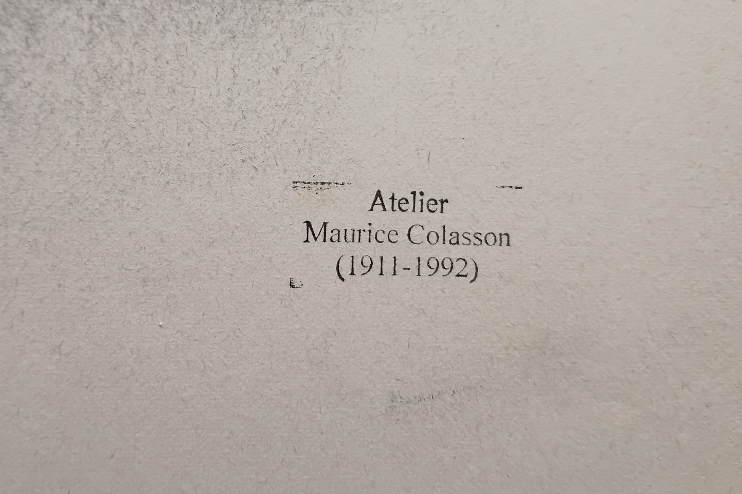 A close-up of a textured light grey surface with printed black text reading 'Atelier Maurice Colasson (1911-1992)'.