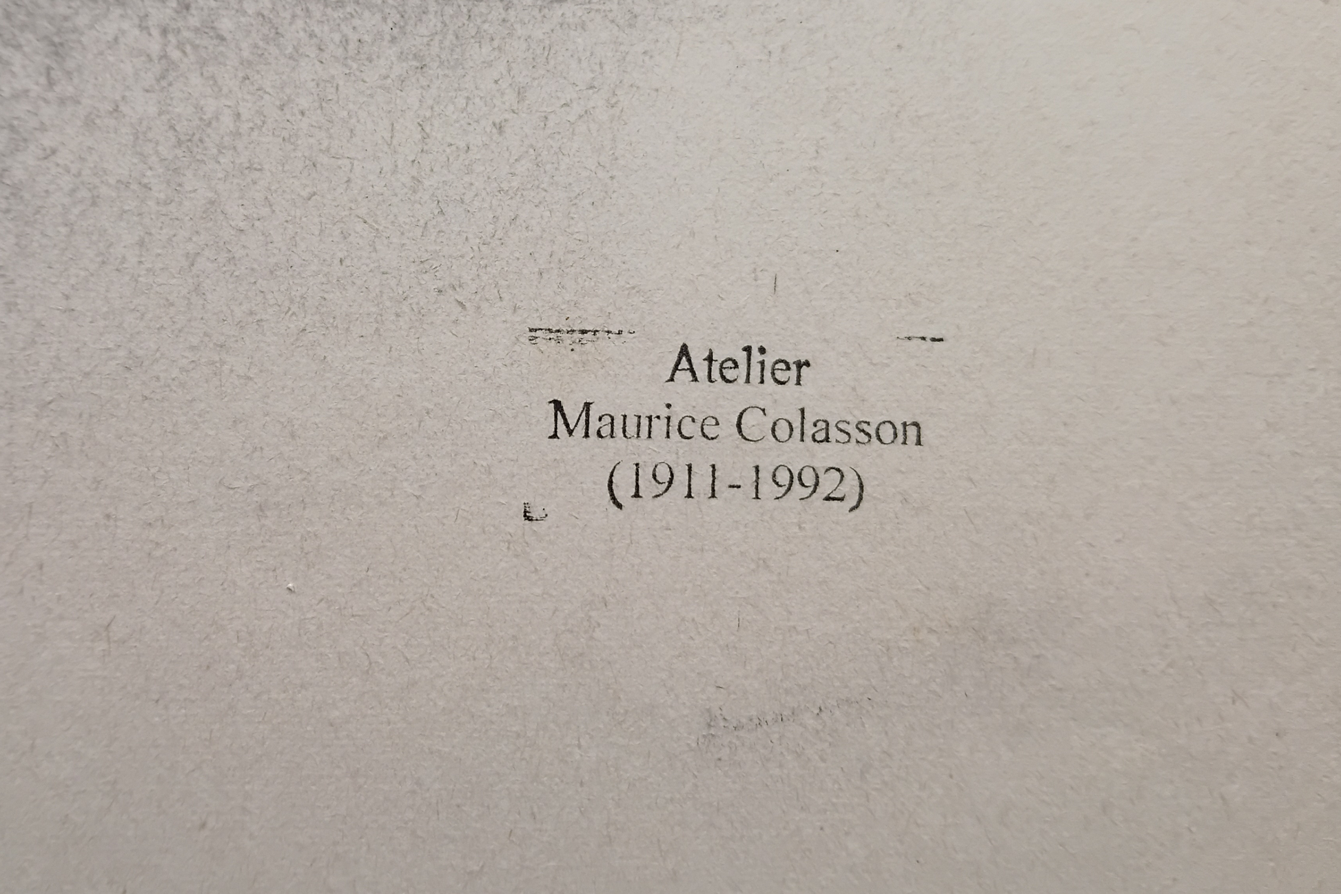 A close-up of a textured light grey surface with printed black text reading 'Atelier Maurice Colasson (1911-1992)'.