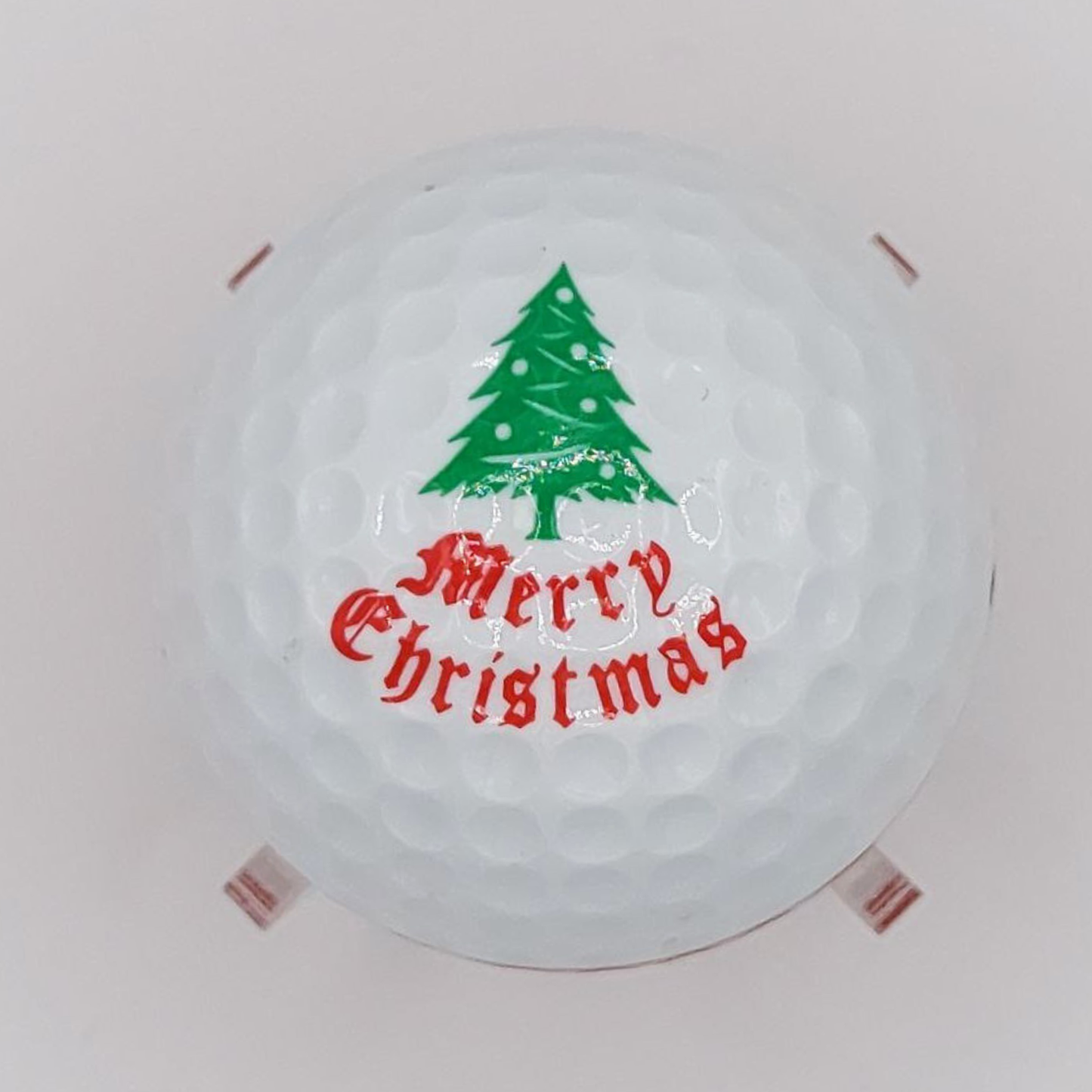 Round white golf ball with a green Christmas tree and red 'Merry Christmas' text on a white background