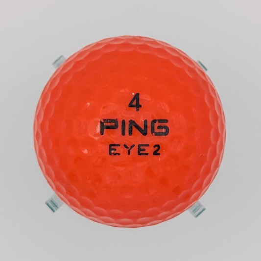 A vintage orange coloured golf ball on a plastic stand. 