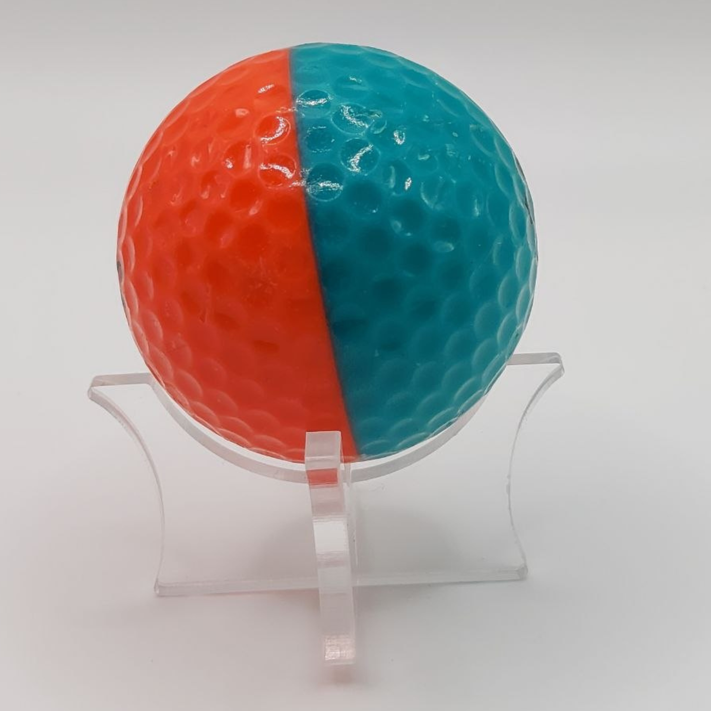 Half orange, half teal vintage golf ball on a clear stand against a white background