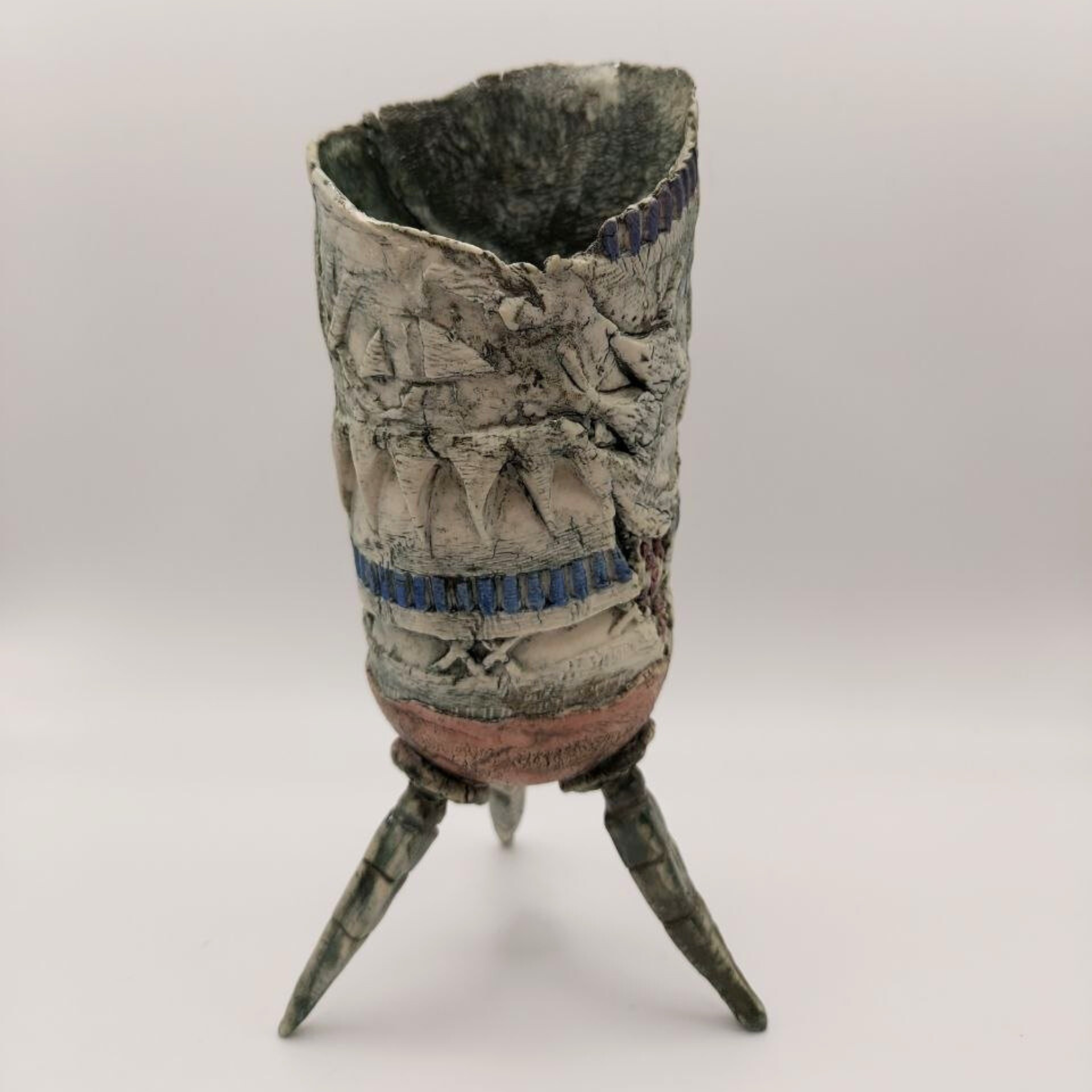 Textured ceramic vase with three legs on a white background