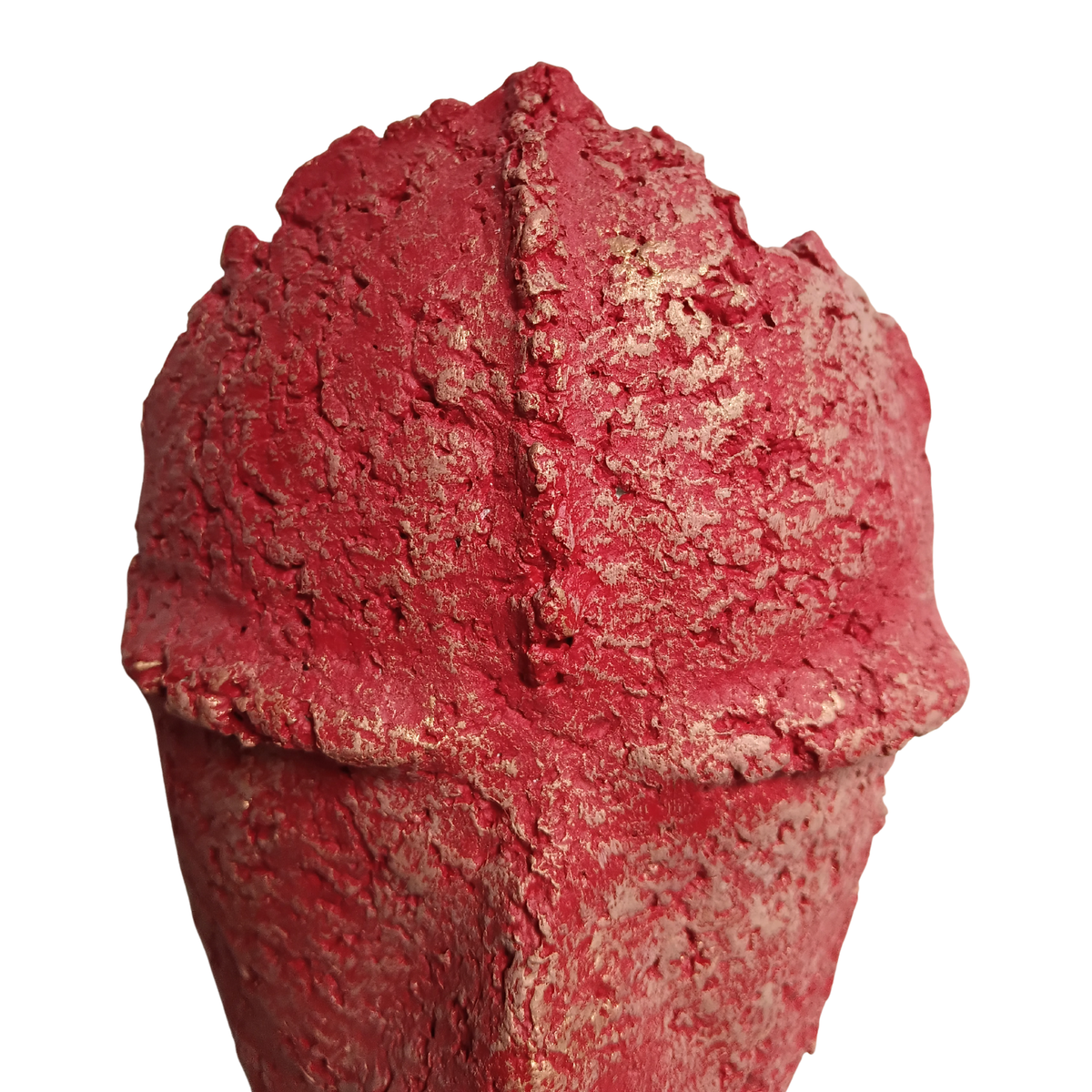 A close-up of a textured red mask sculpture with a rough, cracked surface and a central ridge, shown against a plain white background.