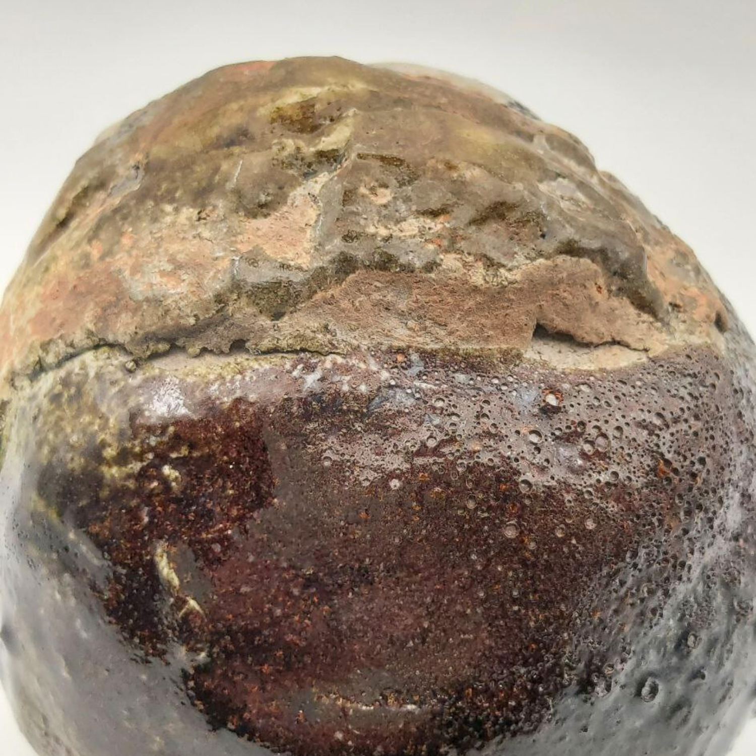 Close-up of a textured, brownish sculpture with a rough surface on a white background