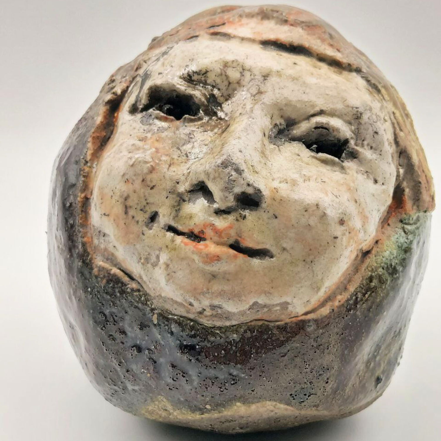 Ceramic face sculpture with a neutral expression on a white background
