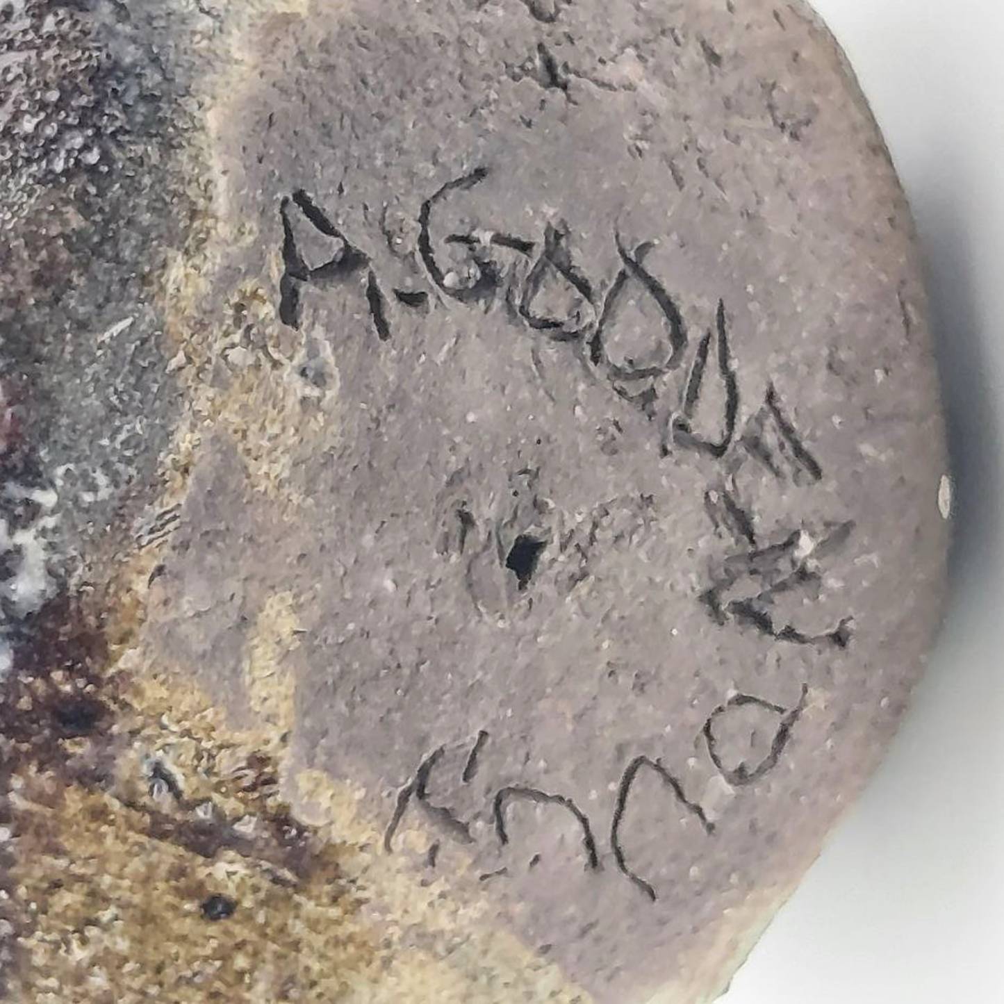 Close-up of a textured sculpture head with engraved text "A. Godden" on a white background