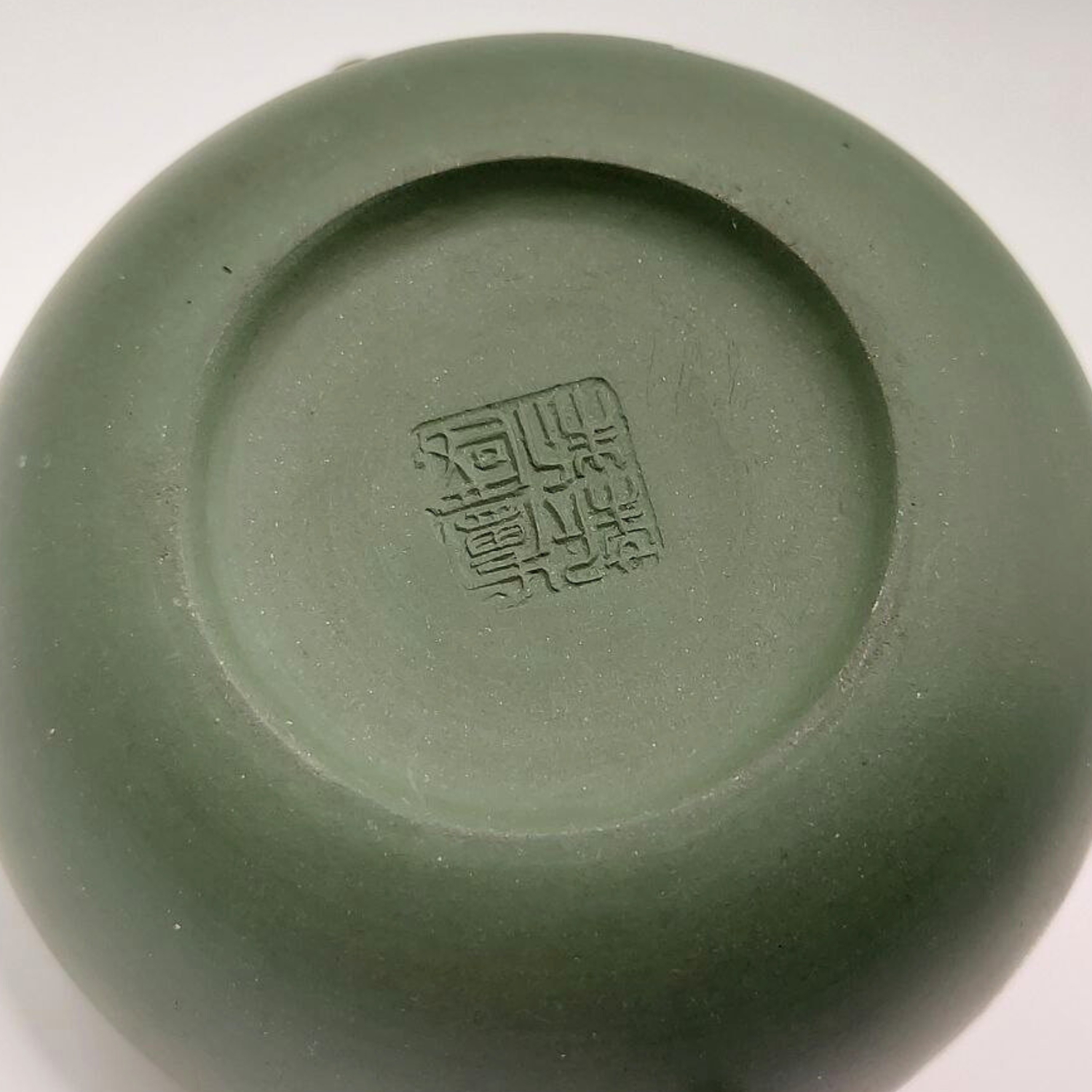 A green mini Chinese clay teapot with maker's mark on a white background