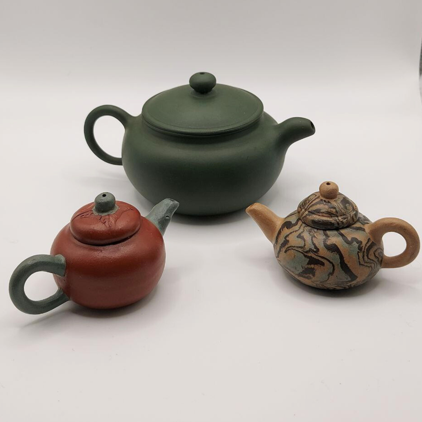 Three miniature Chinese Yixing clay teapots on a white background