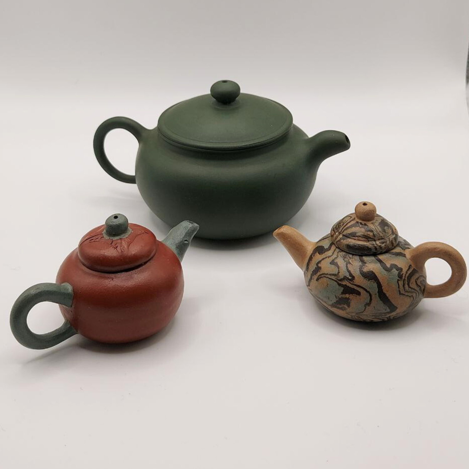 Three miniature Chinese Yixing clay teapots on a white background