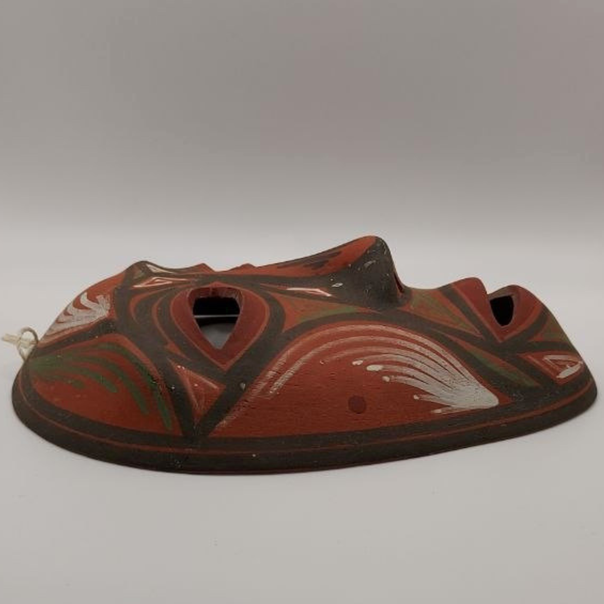 Ceramic mask with red and green design on a grey background