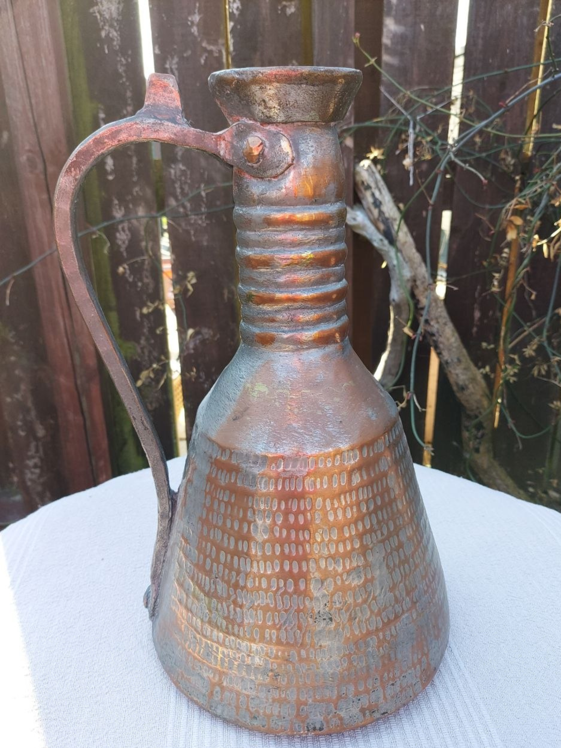 A copper water jug on a table outside. 