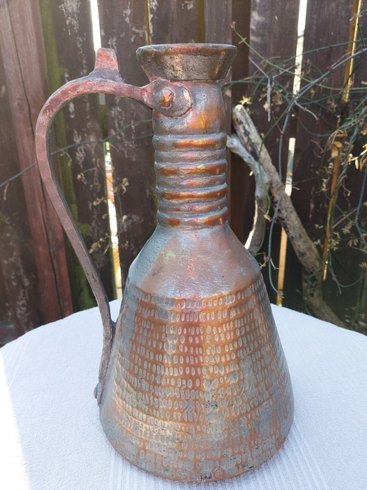 A copper water jug on a table outside. 