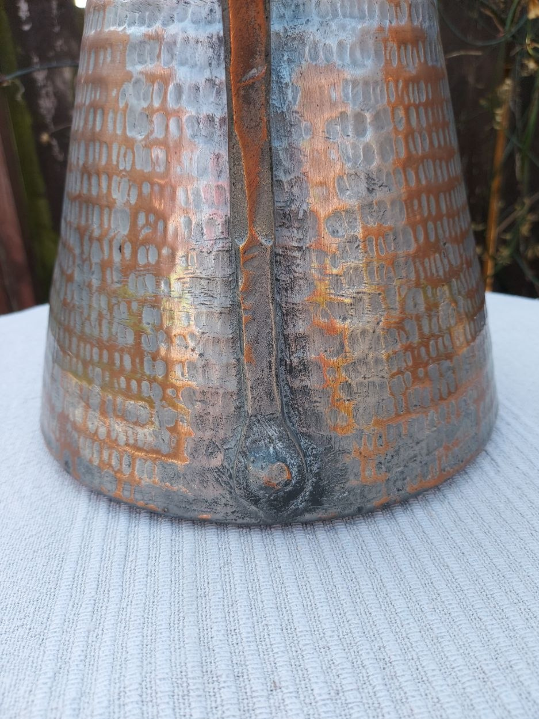 Textured copper water jug with patterns on a white tablecloth. 