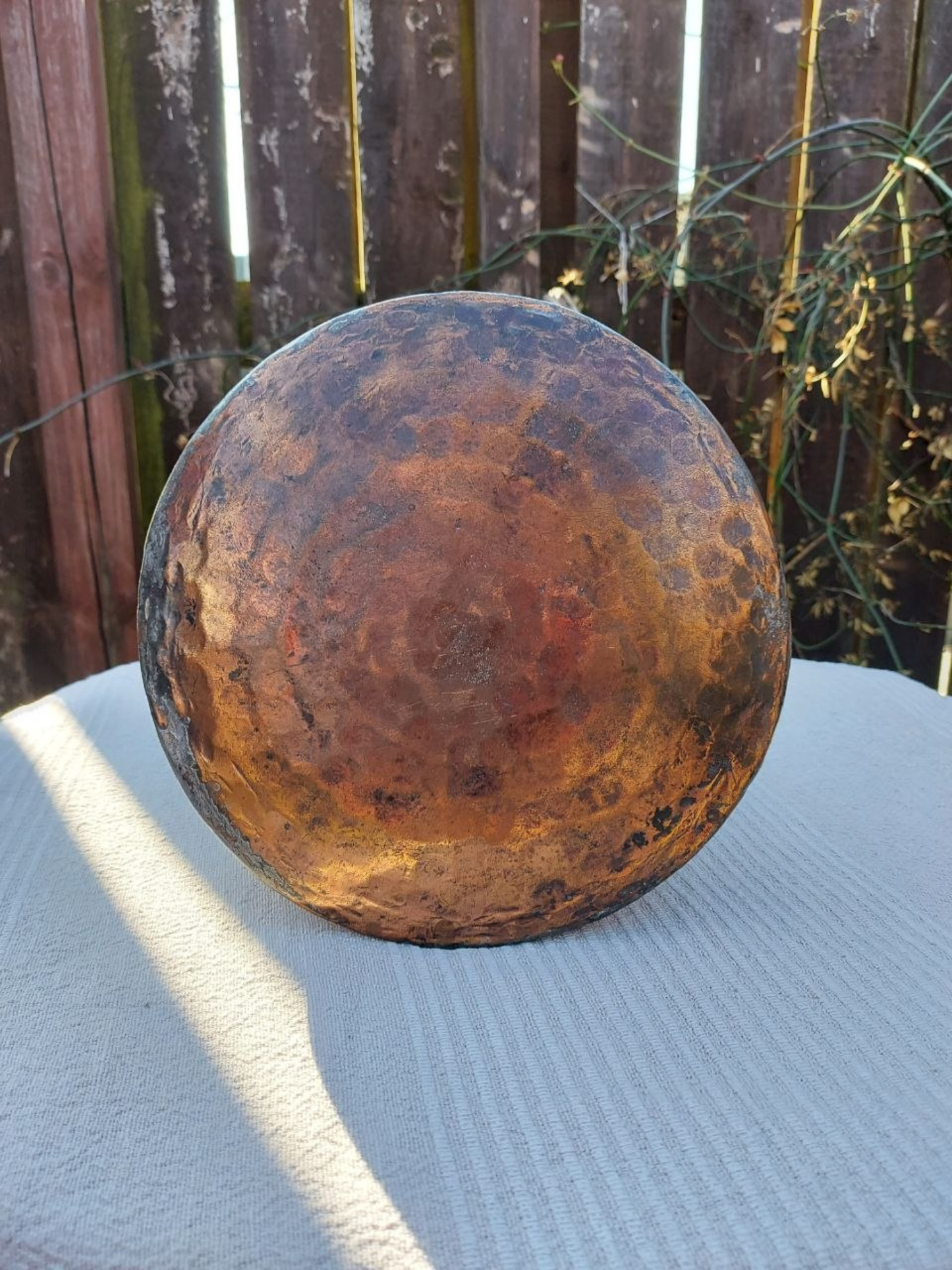 Base of a copper water jug with a wooden fence background