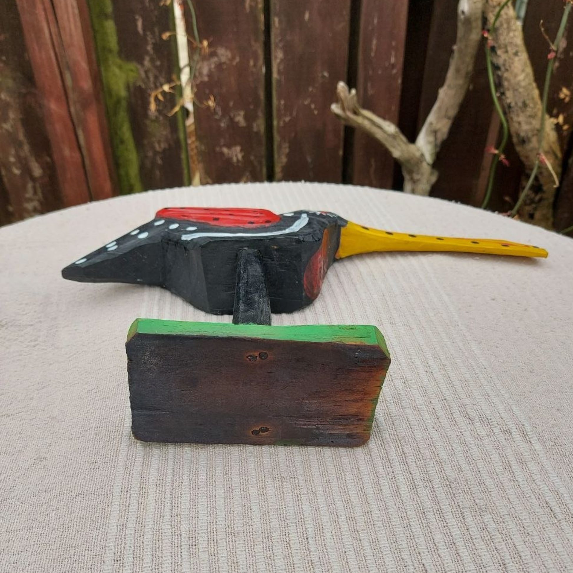Wooden toucan sculpture with a red head and yellow handle on a textured surface.
